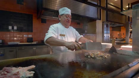 Older-Adult-male-Mexican-Chef-cooking-chicken-on-a-grill-and-transferring-it-to-a-plate