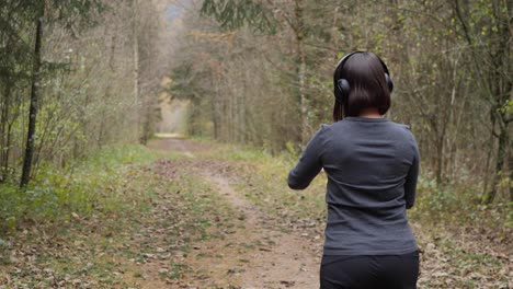 Woman-puts-on-her-headphones,-activates-her-fitness-app-on-the-smartwatch-and-starts-her-run-through-the-forest---American-backview