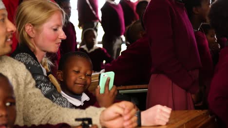 Black-student-in-African-school-looks-at-white-adult-woman-phone