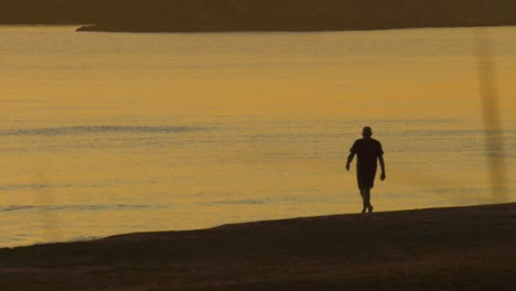 Silhouette-of-middle-aged-man-walking-on-peaceful-sea-shore-at-dawn,-slow-motion