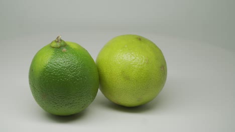 Zwei-Reife-Grüne-Zitrusfrüchte-Limettenrotation-Im-Uhrzeigersinn-Auf-Dem-Drehteller-Mit-Weißem-Hintergrund---Nahaufnahme