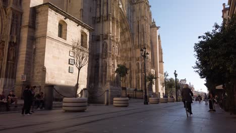 Herunterschwenken-Der-Kathedrale-Von-Sevilla-Mit-Radfahrer,-Der-Auf-Dem-Fahrrad-Vorbeifährt