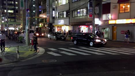 Gente-Cruzando-La-Calle-Por-La-Noche-Mientras-Un-Coche-Se-Detiene-Para-Dejarles-Pasar,-Toma-Manual