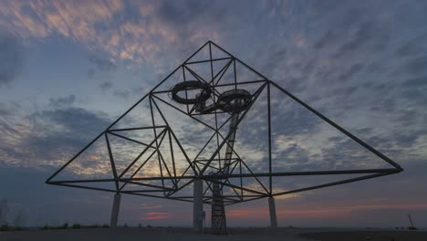 Lapso-De-Tiempo-Del-Amanecer,-Silueta-De-Pirámide-De-Acero-Tetraeder-Contra-Nubes-Coloridas