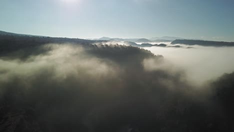Vista-Aérea-De-Bosques-Cubiertos-Entre-Nubes,-Hermoso-Cielo-Azul-Con-Sol
