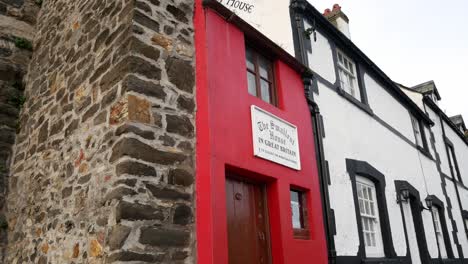 Tiny-small-red-tourism-landmark-house-on-Wales-Conwy-harbour-closed-during-covid-lockdown-low-angle-dolly-right