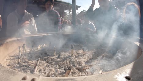 Close-up-of-a-large-pot-with-burning-incense-sticks-ans-ash