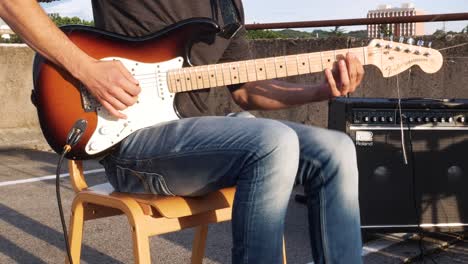 Closeup-of-guitar-player-playing-electric-guitar-on-top-of-the-parking-garage,-with-visible-apartment-blocks-and-some-tree-tops-in-the-background