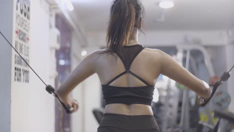 Backside-of-strong-athlete-girl-exercising-and-working-out-with-cables-and-pulleys-at-gym,-slow-motion,-sweat-due-to-hard-work-out