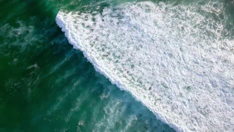 Surfer-ducks-under-a-crashing-wave-in-Dreamland-beach-Bali-Indonesia,-Top-view-rotating-shot