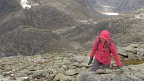 A-Woman-Smiles-as-She-Hikes-up-a-Steep-Rocky-Landscape-on-a-Cold,-Overcast-Day-in-Norway,-Slow-Motion