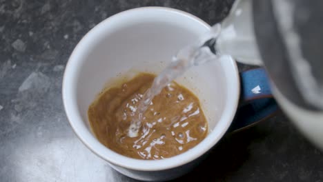 Pouring-hot-water-into-a-mug-of-instant-coffee-in-slow-motion