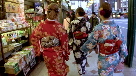 Toma-En-Cámara-Lenta-Por-Detrás-De-Tres-Mujeres-Japonesas-Caminando-Y-Usando-Kimono-Tradicional-En-La-Calle-De-Kyoto-Japón