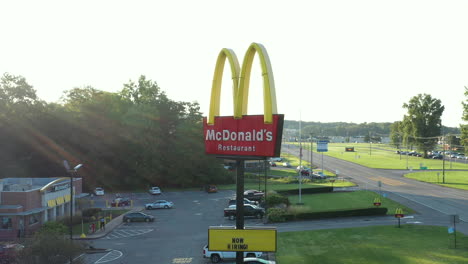 Drone-orbit-of-McDonald's-sign-and-restaurant-building-at-sunrise-with-sun-flare