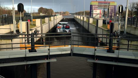 Frachtschiff-Fährt-Ins-Eefde-schleusentor-Ein,-Schließt-Die-Türen,-Wasser-Steigt-Auf-Und-Fährt-An-Einem-Bewölkten-Tag-Mit-Einem-Regenbogen-Am-Ende-Auf-Dem-Twentekanaal-Fort