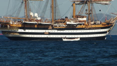 Most-beautiful-ship-in-the-world,-Amerigo-vespucci-ship-in-gulf-of-Palmas,-south-Sardinia,-small-boat-with-tourists-passing-by,-static,-windy-day
