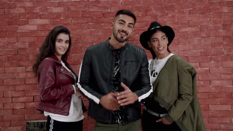 A-Man-And-Two-Women-Posing-In-Front-Of-Brick-Wall-Wearing-Urban-Clothing---Medium-Shot