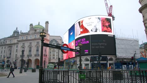 Lockdown-in-London,-one-loan-walker-in-empty-Piccadilly-Circus-in-front-of-LED-signage-announcing-"we'll-get-through-this-together"-COVID-19-messages