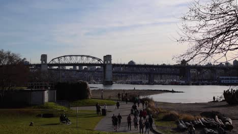 People-walking-and-running-at-the-sunset-beach-Park-at-the-English-bay-in-Vancouver-enjoying-the-calm-sunny-winter-day-with-the-Granville-bridge-at-the-background