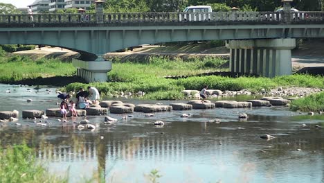 Japanische-Kinder-Spielen-An-Einem-Sonnigen-Tag-Gerne-Auf-Den-Trittsteinen-Am-Kamogawa-Fluss-In-Kyoto,-Japan