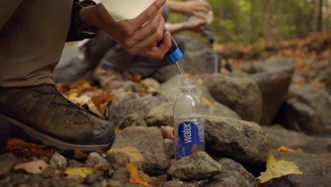 A-Hiker-Filtering-Clean-Water-into-a-Water-Bottle-Next-to-a-Stream-in-a-Forest-with-Beautiful-Fall-Colors
