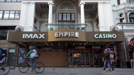 Una-Toma-En-Cámara-Lenta-De-Personas-Paseando-En-Bicicleta-Y-Pasando-Por-El-Cine-Imperio-Imax-Tapiado-En-Leicester-Square-Durante-El-Segundo-Cierre-Nacional-De-Coronavirus