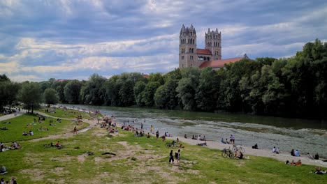 Summer-in-Munich,-Germany,-People-on-Isar-River-Rivebank,-View-on-St