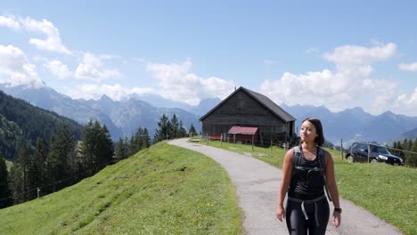 Hübsche-Frau,-Die-An-Sonnigen-Tagen-Auf-Dem-Ländlichen-Weg-Mit-Wunderschönen-Alpenbergen-Im-Hintergrund-Wandert