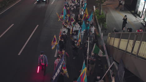 Asian-Protesters-Wearing-Masks-And-Waving-Flags-As-They-March-On-The-Street-In-Tokyo,-Japan-At-Night---Solidarity-With-Hong-Kong-Protest---high-angle,-static-shot