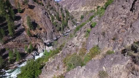 Flying-over-a-steep-and-rugged-canyon-with-a-river-and-waterfall-below