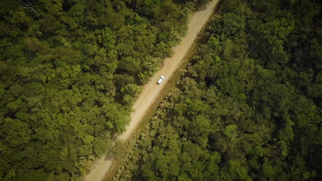 Aerial-view-of-a-car-driving-on-a-dirt-road-in-a-tropical-rainforest