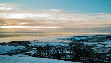 Cloud-inversion-covering-the-Eden-Valley-in-Cumbria-with-the-Lakeland-mountains-in-the-background,-and-the-sun-breaking-through-the-clouds-and-lighting-up-trees-in-the-foreground