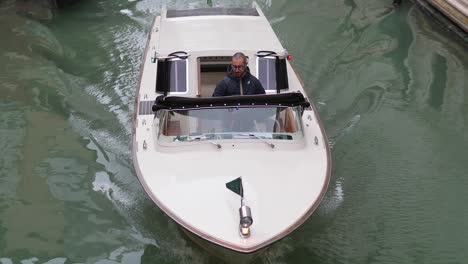 El-Hombre-Dirige-Una-Lancha-De-Lujo-En-El-Canal-De-Venecia,-El-Agua-De-La-Marea,-Entre-El-Edificio-Antiguo-Y-Varias-Góndolas.