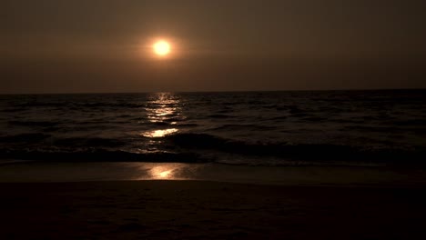 Dunkler-Sonnenuntergang-Mit-Meer-Im-Vordergrund-Und-Wellen,-Die-Den-Strand-Treffen