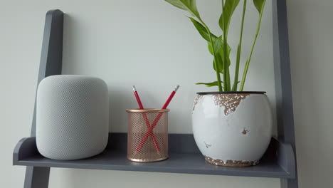 Toma-Panorámica-En-Cámara-Lenta-De-Un-Hombre-Golpeando-Un-Homepod-De-Apple-En-La-Parte-Superior-De-Una-Estantería-De-Aspecto-Moderno-Junto-A-Un-Portalápices---Planta