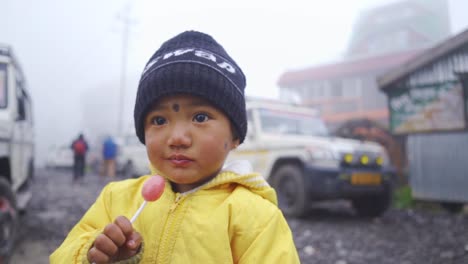 Cute-innocent-little-Asian-child-looking-at-camera-with-lollipop-at-foggy-winter-morning,-slow-motion