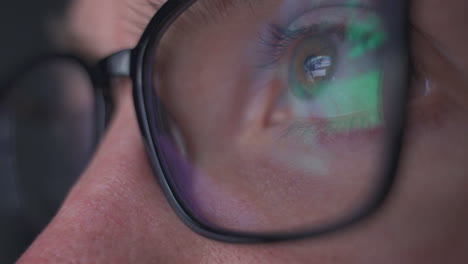 Close-up-macro-view-of-young-man-in-glasses-eye-moving-fast-staring-at-video-games-and-the-bright-screen-of-a-computer-with-colorful-flashes