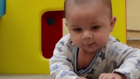 cute-tree-months-old-baby-boy-making-funny-faces-while-having-tummy-time-outside-in-front-of-plastic-colorful-play-house