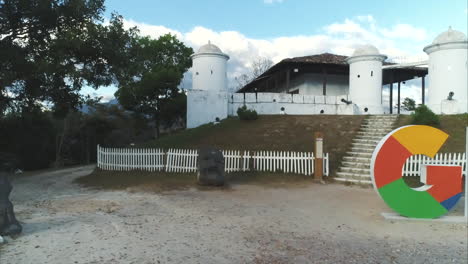 Toma-Panorámica-Horizontal-Baja-De-Un-Cartel-Con-Letras-Grandes-Frente-A-La-Fortaleza-Histórica-En-Gracias,-Honduras