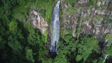 Aerial-view-of-a-waterfall-and-a-cliff-at-sunset-with-lush-green-forest-in-the-foreground-and-background