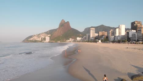 Aerial-fly-over-view-of-coastal-city-beach-of-Rio-de-Janeiro-during-early-morning-golden-hour-sunrise-with-a-few-people-enjoying-the-lovely-start-of-the-day