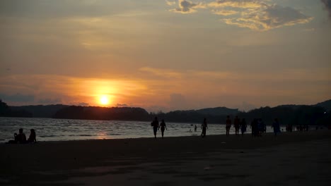 Ao-Nang-Beach-Zeitraffer,-Während-Die-Sonne-über-Den-Bergen-Im-Hintergrund-Untergeht,-Während-Touristen-Und-Einheimische-Den-Strand-Bedecken,-Um-Den-Wunderschönen-Sonnenuntergang-In-Krabi-Thailand-Zu-Beobachten