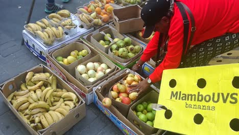 Una-Vendedora-Ambulante-Afroamericana-Empacando-Fruta-Para-Un-Cliente-En-Un-Mercado-Callejero-En-El-Centro-De-Ciudad-Del-Cabo.