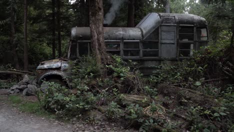 Old-Bus-with-GMC-insignia-being-used-as-a-home-in-the-woods-of-Vancouver-Island,-Canada,-a-furnace-is-being-used-inside,-dolly-pan-reveal-shot