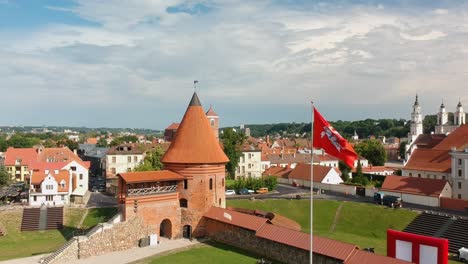 Toma-Aérea-Subiendo-Enfocada-En-La-Torre-Principal-Y-Una-Bandera-Roja-Del-Castillo-De-Kaunas