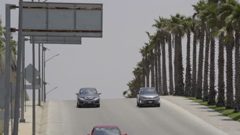 Coches-Circulando-Por-Un-Bache-A-Lo-Largo-De-Una-Carretera-Bordeada-De-Palmeras