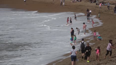 Eine-Gruppe-Von-Menschen,-Die-An-Einem-Strand-Neben-Dem-Meer-Stehen-Und-Laufen