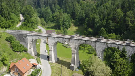 Toma-Aérea-De-Tiro-Inclinado-Para-El-Antiguo-Puente-Ferroviario-Con-Arcos-En-El-Campo-En-Ravne-Na-Koroskem,-Eslovenia