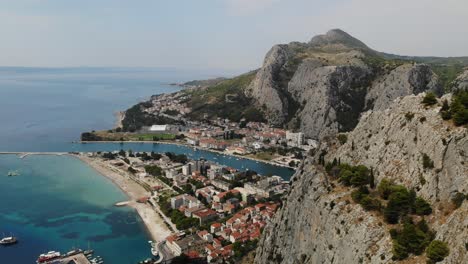 Hazy-sunny-summer-day-aerial-reveal-footage-over-Omis-town,-river-Cetina
