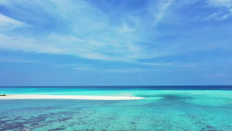 Peaceful-seascape-with-calm-clear-water-of-turquoise-lagoon,-coral-reef-patterns-under-water-and-blue-sky-with-white-clouds-in-Maldives